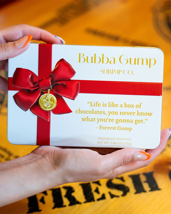 Bubba Gump Shrimp Co. box of chocolates tin with a red bow held by a hand.