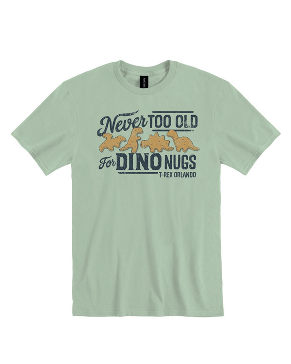 A light green crewneck T-shirt with a design on the front featuring four dinosaur-shaped chicken nuggets and text around it that reads: "Never TOO OLD for DINO NUGS - T-REX ORLANDO". the background is plain white.