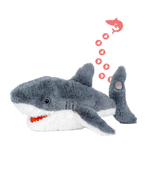A grey shark plush toy with a white underbelly and an open mouth. There is an illustration above the shark depicting a smaller shark icon with several small red hearts trailing behind it, leading to a target symbol on the side fin of the plush toy. The background is plain white.
