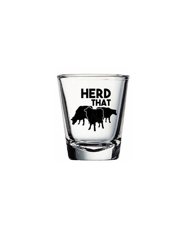 A shot glass that reads "herd that" in the center and three black cow silhouettes under it. The background is plain white.