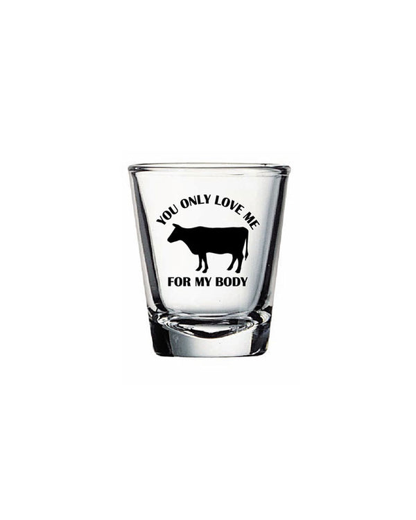 A clear shot glass that reads "You only love me for my body", surrounding a black cow silhouette in the center. The background is plain white.