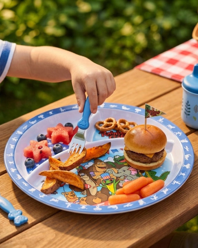 Child's hand with a fork over a plate of food on a wooden table outdoors.