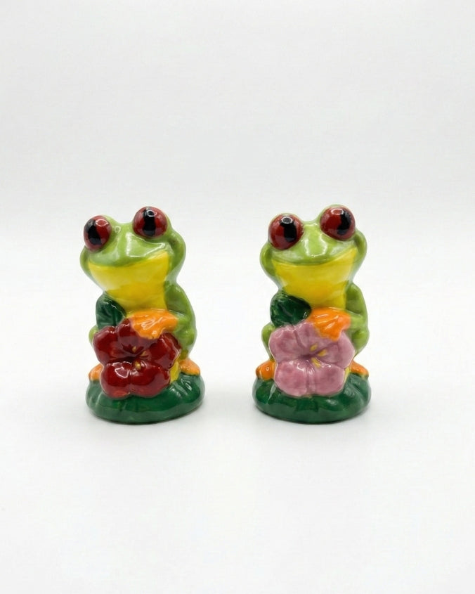 Two ceramic frog figurines with flowers on a white background