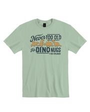 A light green T-shirt with a graphic design on the front featuring four dinosaur-shaped chicken nuggets and text that reads: "Never TOO OLD for DINO NUGS - T-REX ORLANDO".