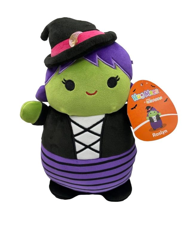 A plush toy with a green face, purple hair, and a black witch’s hat adorned with a pink band and a small skull. The toy is wearing a black outfit with white criss-cross patterns on the chest and purple and black striped leggings. It is holding up one hand and has an attached tag featuring the word ‘Squishmallows’ with an illustration of the same character named Rosalyn.