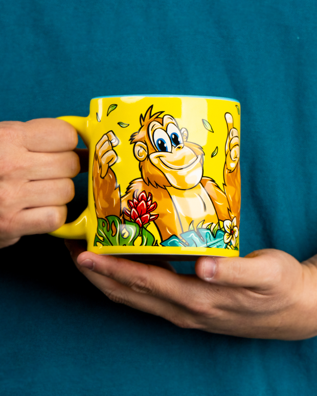 Person holding a yellow mug with a cartoon orangutang design against a blue background