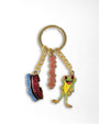 A gold-tone metal keychain featuring three colorful enamel charms: a blue and red train, a pink script charm, and a green and yellow frog, set against a plain white background.