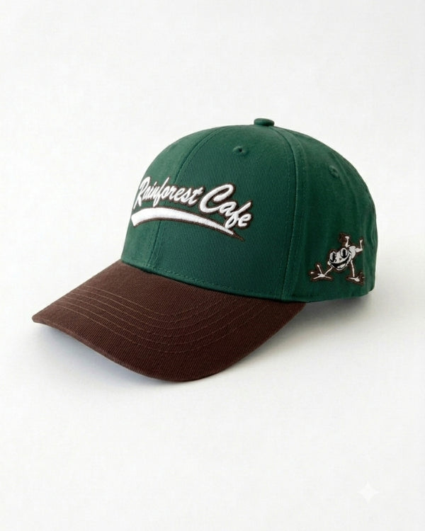 A structured baseball cap with a dark green crown, a brown curved brim, and white embroidered text reading 'Rainforest Cafe' on the front, plus a small embroidered logo on the side.