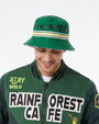 A man wearing a green bucket hat with black animal silhouettes and a green bomber jacket with 'RAIN FOREST CAFE' and 'STAY WILD' graphics, against a plain white background.