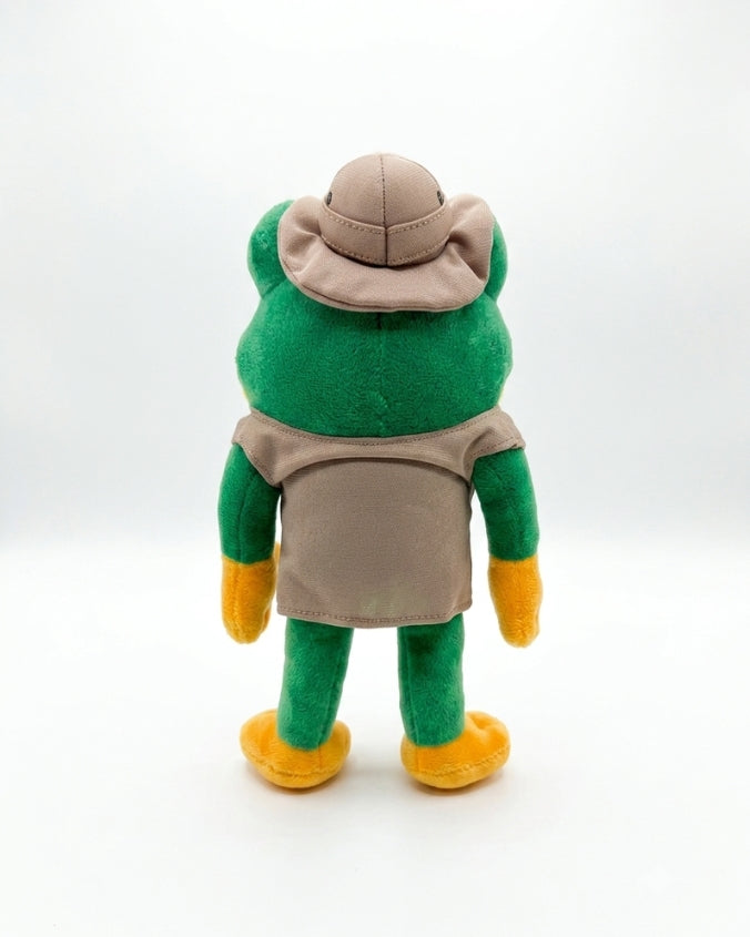 A plush toy frog shown from the back, wearing a tan hat, vest, and apron with green arms and legs, and yellow shoes, photographed on a white studio background.