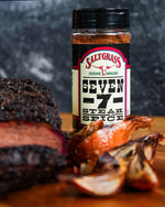 A close-up shot of a spice container of "Saltgrass Steak House Seven 7 Steak Spice", with the "SALTGRASS STEAKHOUSE" logo on it. Next to it is a piece of brisket and onion on a cutting board.