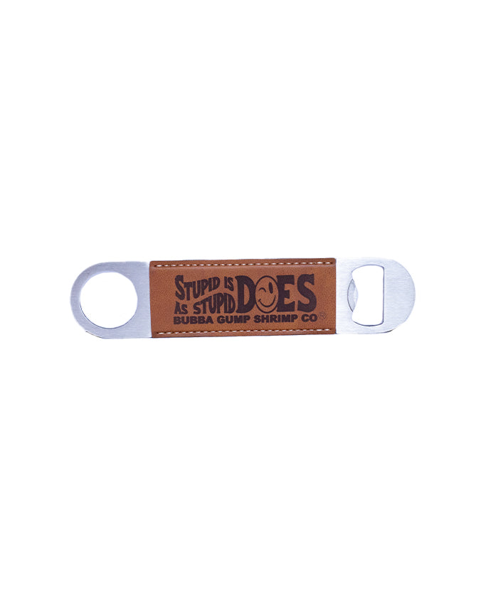 A metal bottle opener with a rectangular brown inset featuring the text ‘STUPID IS AS STUPID DOES’ in darker brown capital letters, followed by ‘BUBBA GUMP SHRIMP CO.’ in smaller darker brown capital letters. The opener has a circular hole on one end and a rectangular opening on the other end for prying off bottle caps