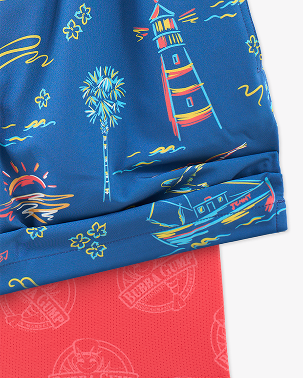 A close-up view of a pair of the corner of a pair of blue shorts with a colorful pattern that includes palm trees, sailboats, lighthouses, and other beach-themed elements. The shorts are lifted to reveal a pink lining with Bubba Gump Shrimp logos on it.