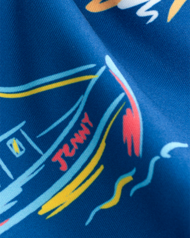 A close-up of blue fabric with a colorful design, including abstract shapes and lines in yellow, red, white, and blue colors. The word "JENNY" is written in red text on an illustrated boat.