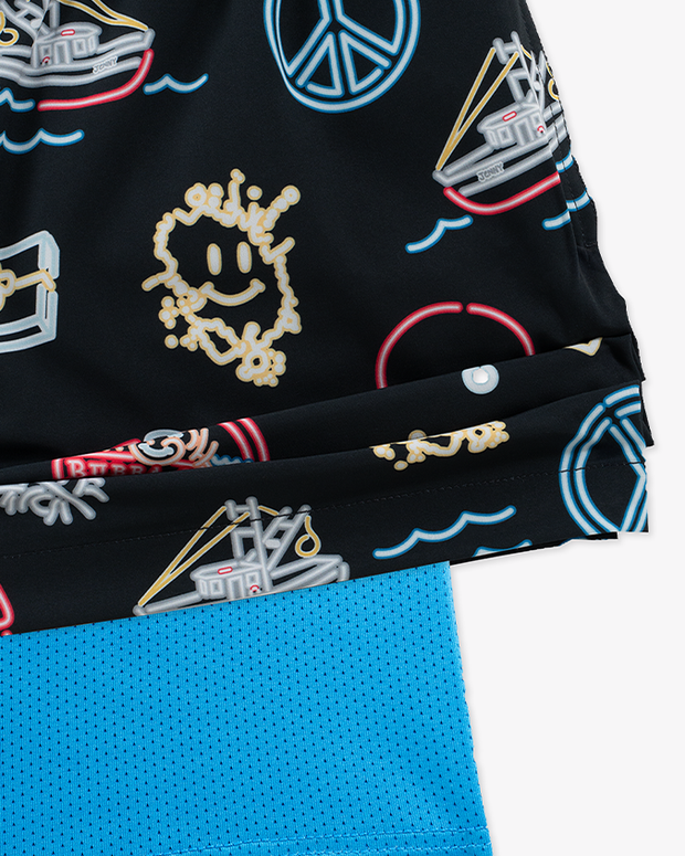 A close-up view of the corner of a pair of black swim shorts with a colorful neon pattern that includes fun paraphernalia including peace signs, ping-pong paddles, boats, etc. The shorts are lifted to reveal a blue mesh lining underneath.