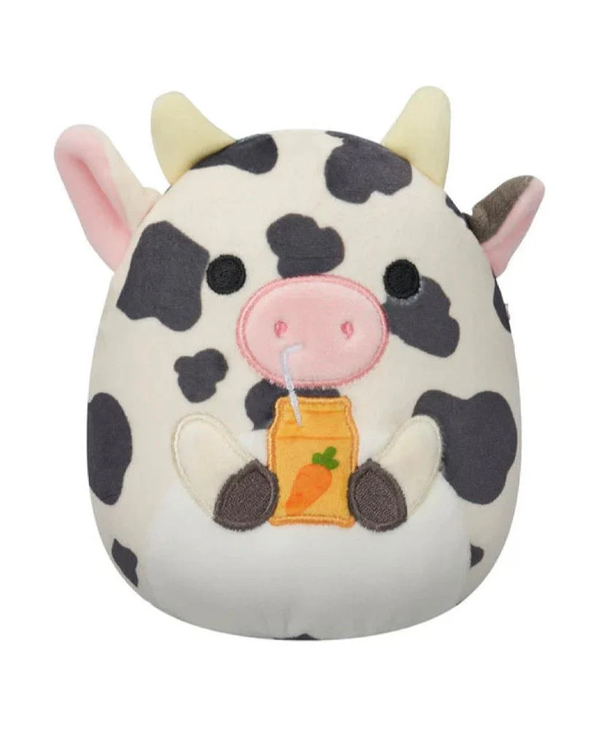 A cute plush cow with black spots, holding a yellow juice carton with a carrot label, and a straw in its mouth.