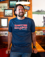 A frontside view of a model in a wooden rustic restaurant wearing a blue crewneck T-shirt, with the text “I’M PRETTY TIRED I THINK I’LL Go Home NOW” – Forrest Gump" in the center in multiple fonts. 