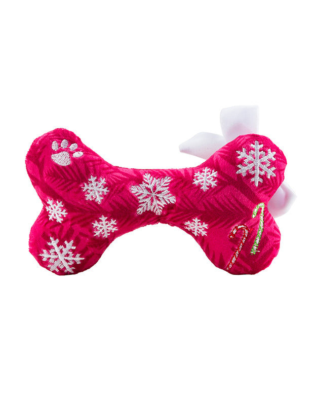  A bright pink dog bone-shaped toy with a plush texture, decorated with white snowflakes and a small white paw print. The toy also features a golden string loop on one end, suggesting it could be used as a holiday ornament. The background is pure white, highlighting the vivid color and details of the toy