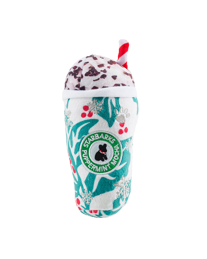 A plush toy designed to resemble a Starbucks Peppermint Mocha, with a white top that imitates whipped cream sprinkled with dark brown spots representing chocolate shavings. The body of the toy features a teal fabric printed with white snowflakes and red berries, along with the Starbucks logo in the center. The toy has a red and white striped straw sticking out from the top.