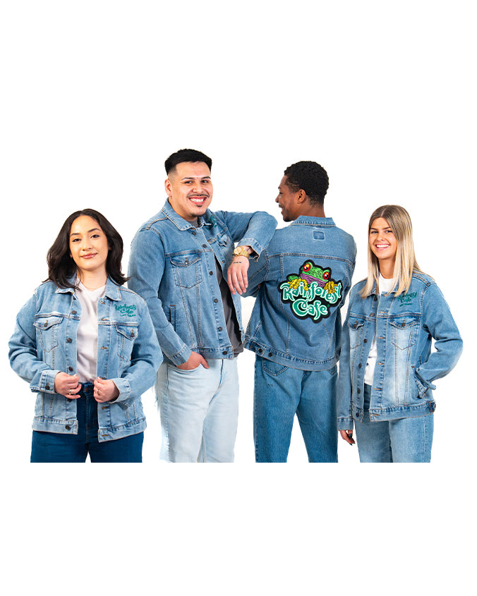 A group of four models' posing and wearing different colored blue jeans and matching blue denim jackets. One person is turned around, showcasing a green embroidered "RAINFROEST CAFE" logo in green with a tree frog above it. The background is plain white.