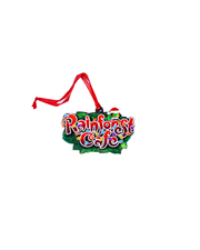 A decorative ornament featuring the text "Rainforest Cafe" in colorful, stylized letters wrapped in rainbow Christmas lights with a frog in a Christmas hat on top, all in front of a patch of green leaves with a red ribbon attached for hanging. The background is plain white.