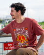 A young man sitting against a railing above a lake and sky, wearing a crewneck t-shirt with the text "BUBBA GUMP Shrimp Co." and "Jenny's Singalong" in cursive with a large peace symbol and floral designs placed in a white frame with stripes inside and flowers around the edges. 