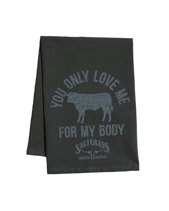 A black cloth with white text reading "You only love me for my body", surrounding a black silhouette in the center, and the "SALTGRASS STEAKHOUSE" logo. The background is plain white.