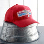 Authentic Forrest Gump cap sitting on top of upside down metal bucket in front of white panel background.